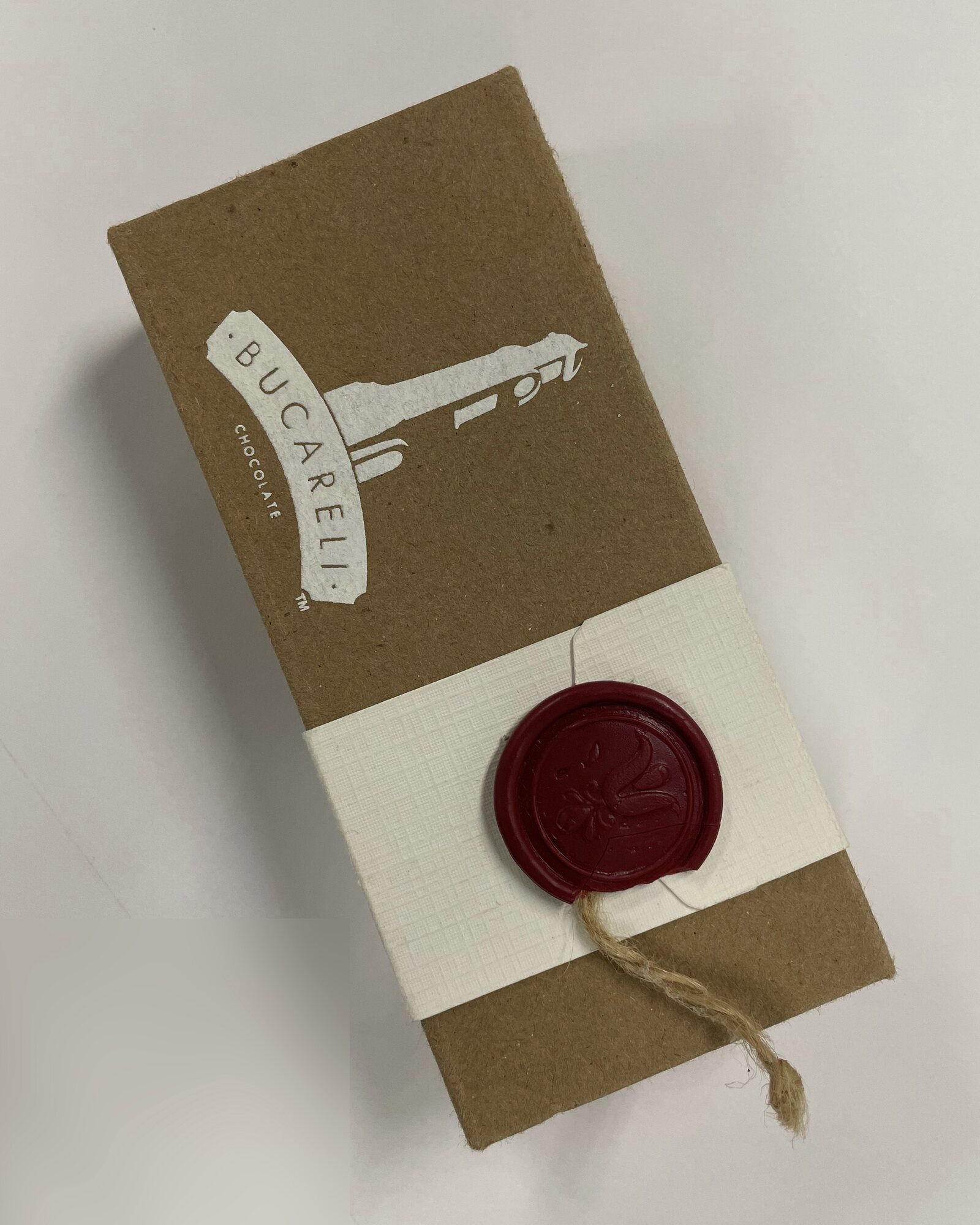 A Bucareli box in kraft board with a white belly band, closed with a red wax seal and twine.